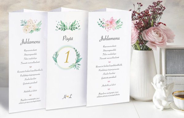 Menukolmio tai menukartio pöydällä kertomaan juhlan ohjelman ja ruokamenun. Kuvassa kukkia ja 3 menukartiota.